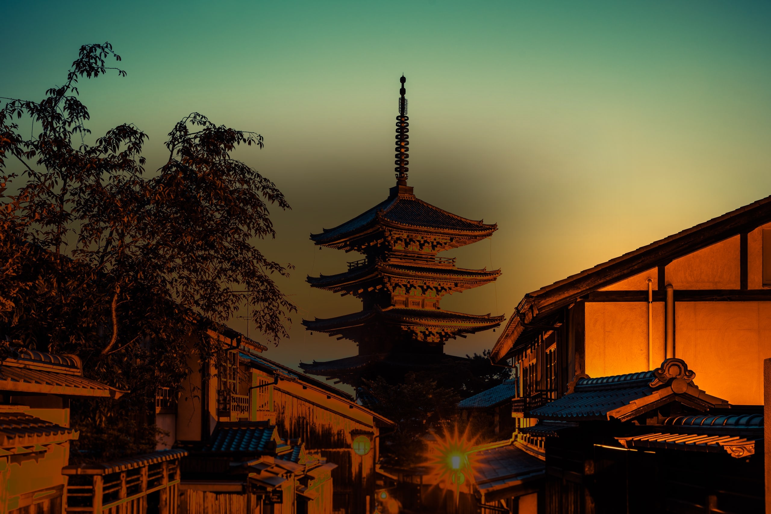 The five-storey Yasaka pagoda silhouetted against the dusk sky above the wooden townhouses of Higashiyama, Kyoto, a street lamp lit below