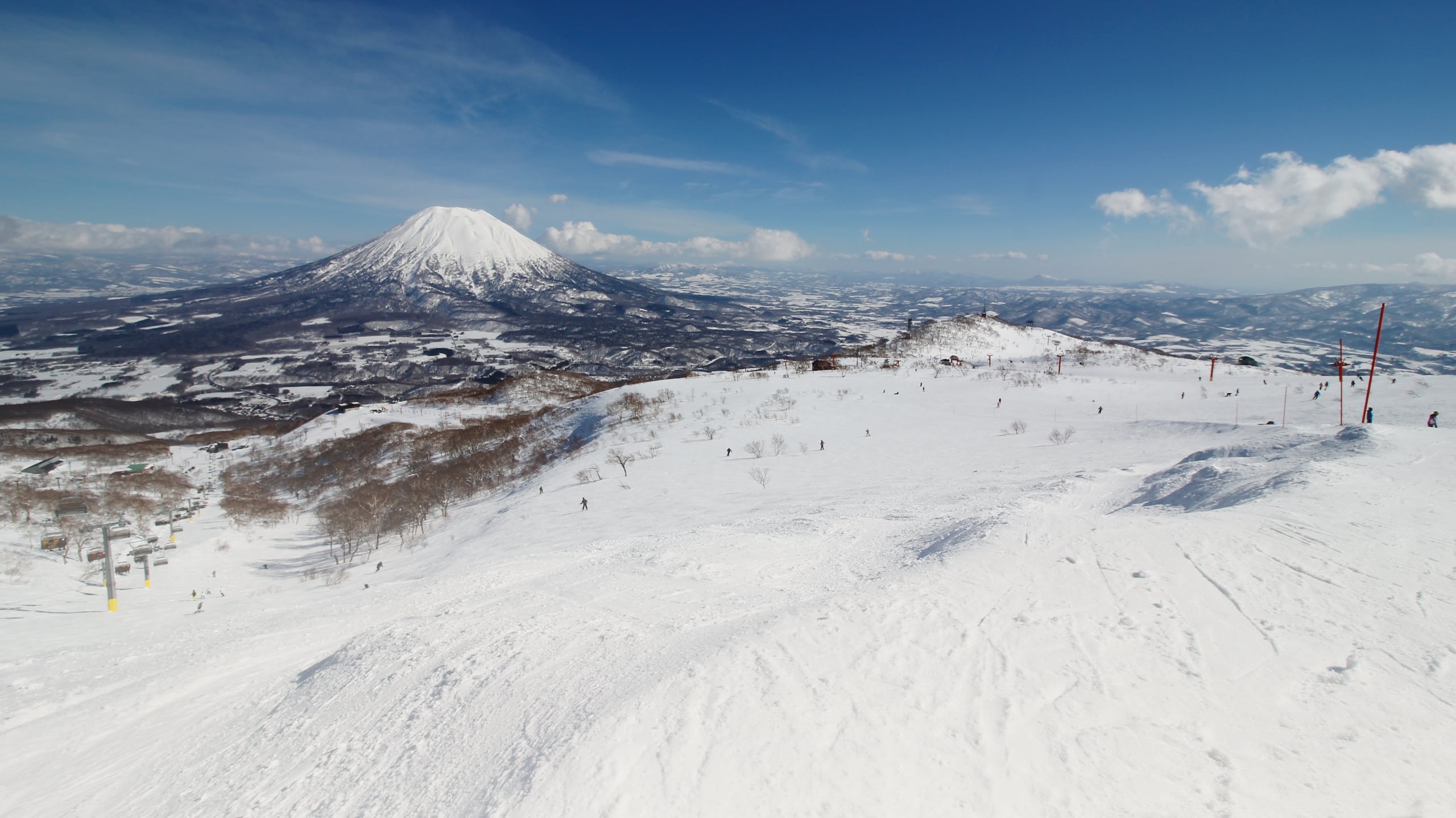 Mount Yotei, a white cone above the plain, seen from the open snow at the top of the Niseko ski area under a blue sky