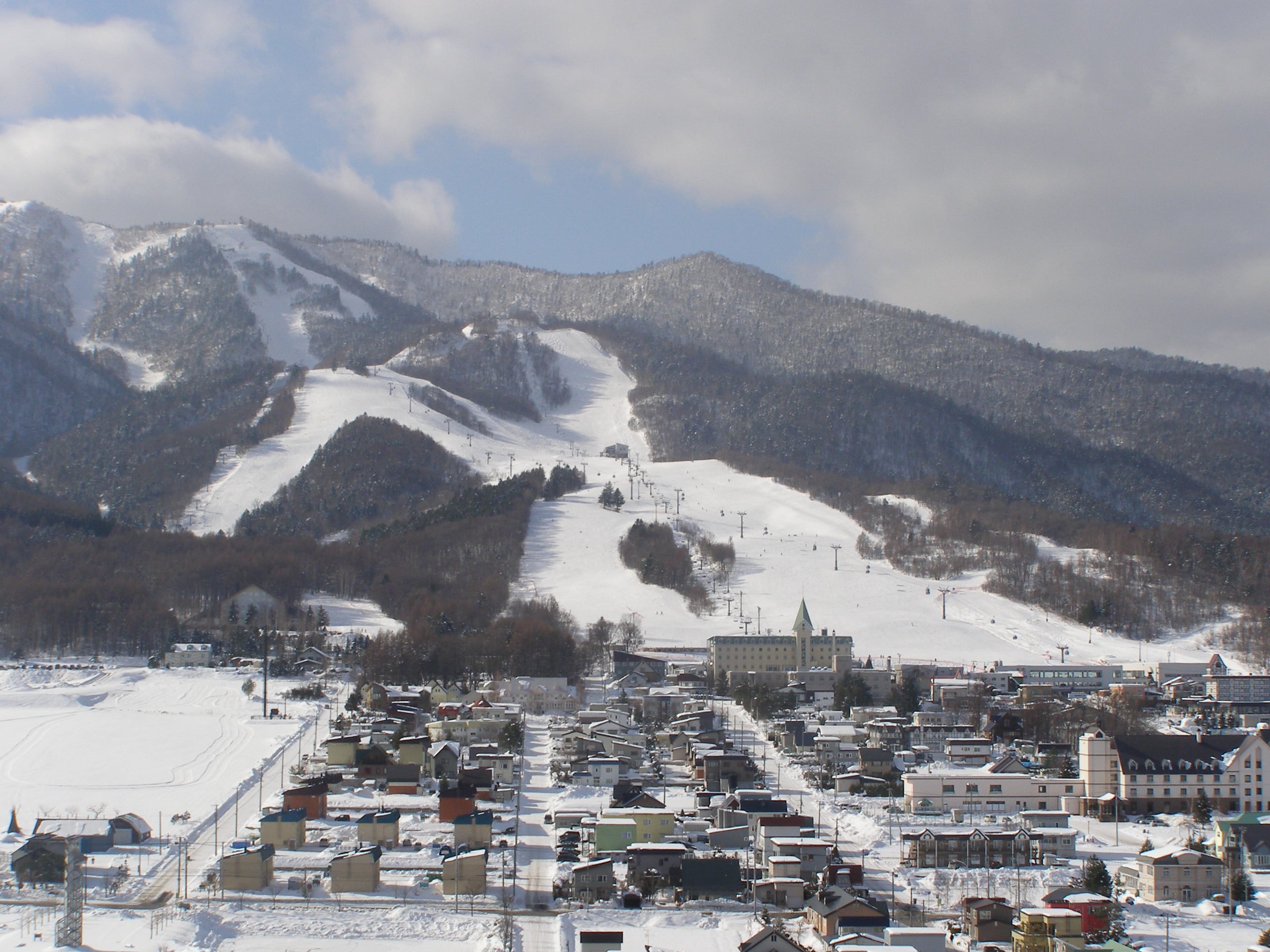 The ski runs of Furano cut white through the forest of the mountain above the snow-covered roofs of the town