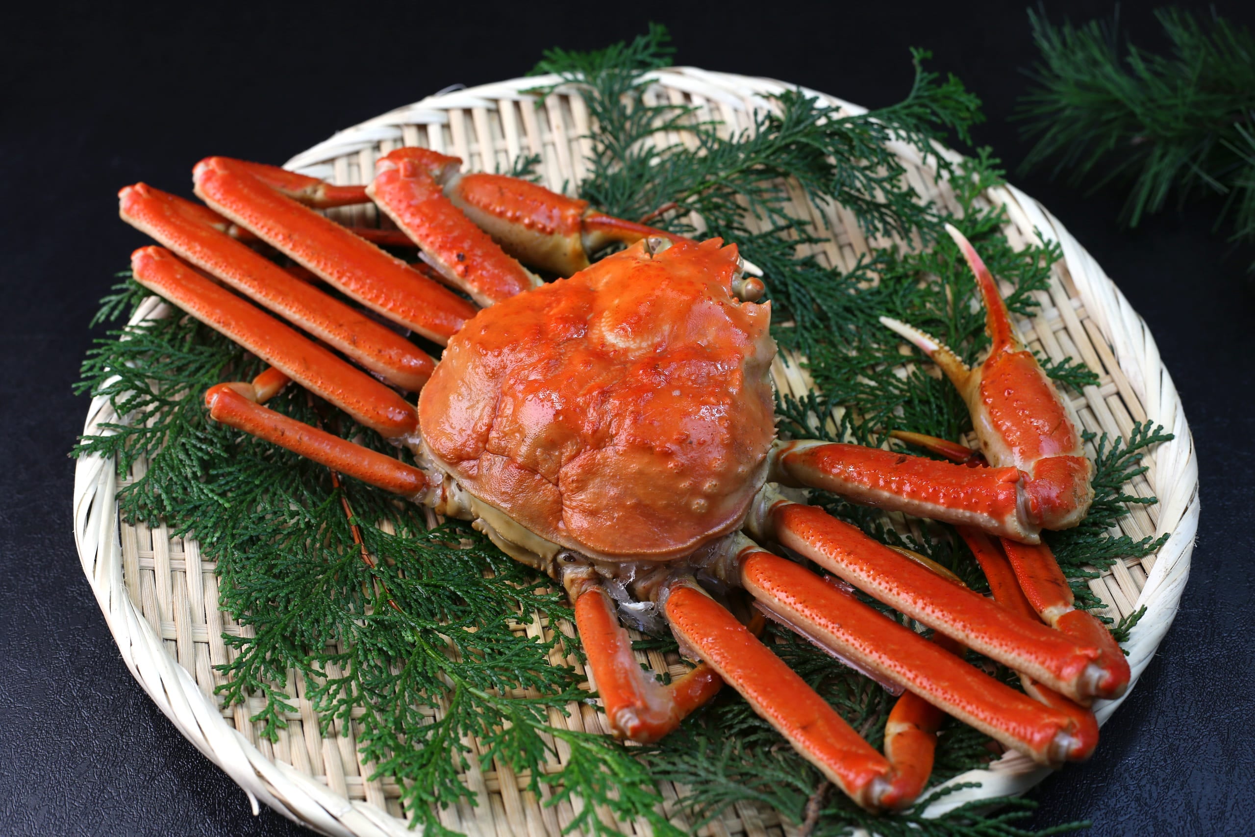 A whole boiled snow crab, its orange legs splayed, on a woven bamboo tray lined with green cedar sprigs