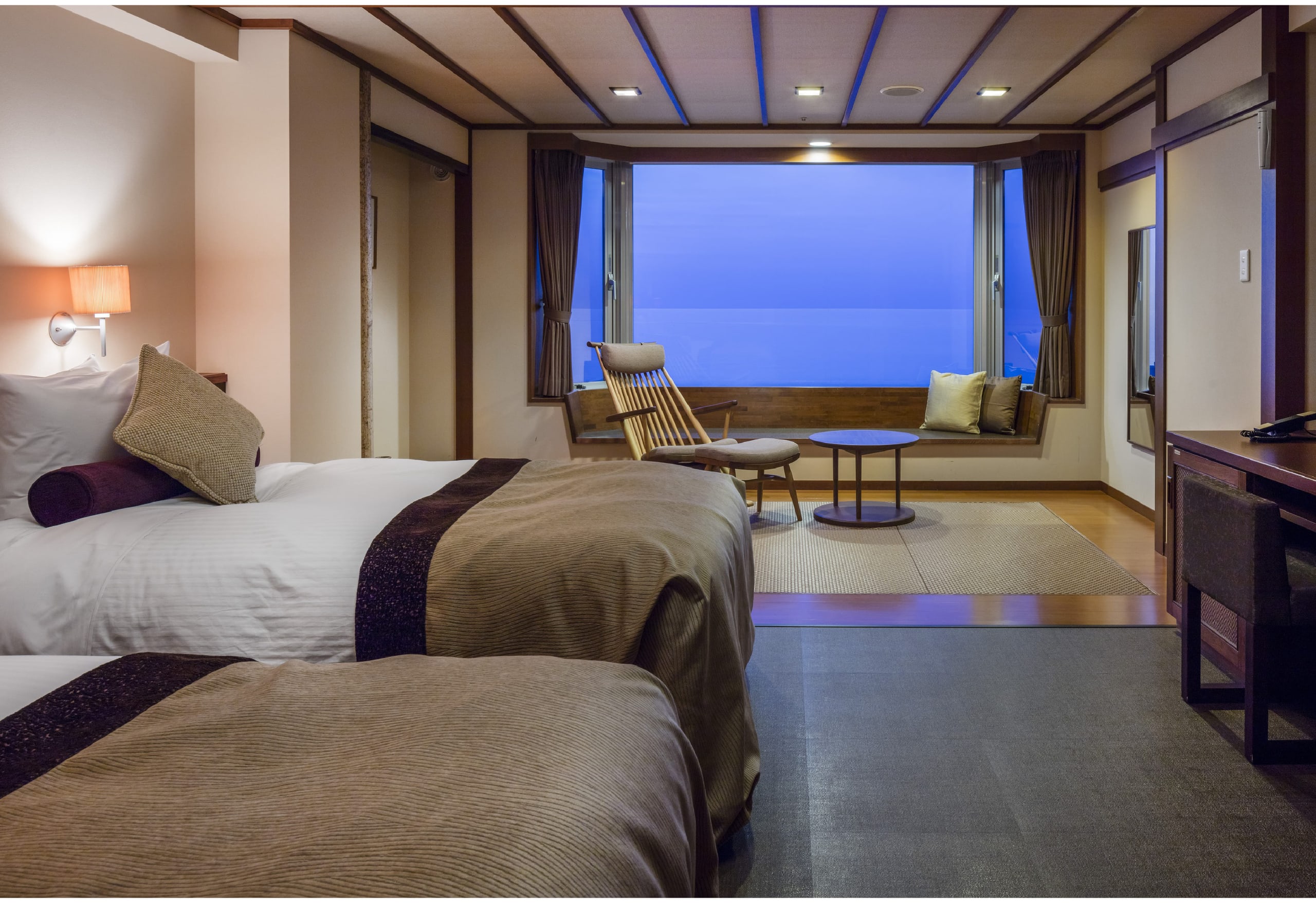 A room at Kitakobushi Shiretoko at dusk, a window seat and a lounge chair before a wide window onto the sea