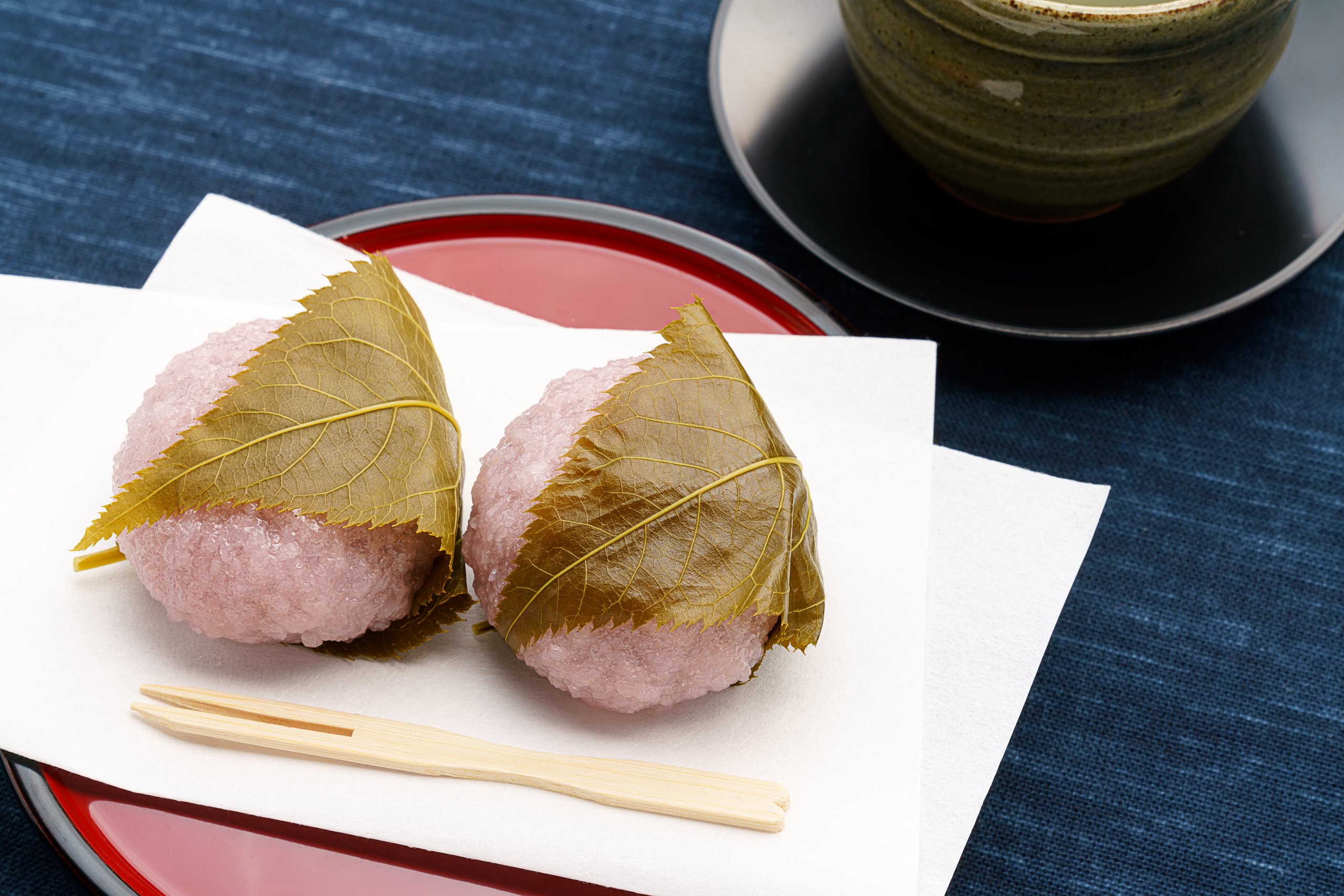 Two sakura mochi wrapped in cherry leaves on a red lacquer plate