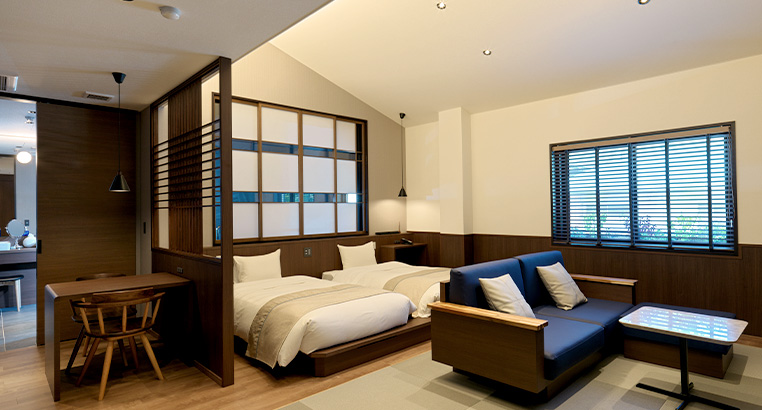 A room in pale wood, a bed and a blue sofa, a shoji screen and a window onto the trees