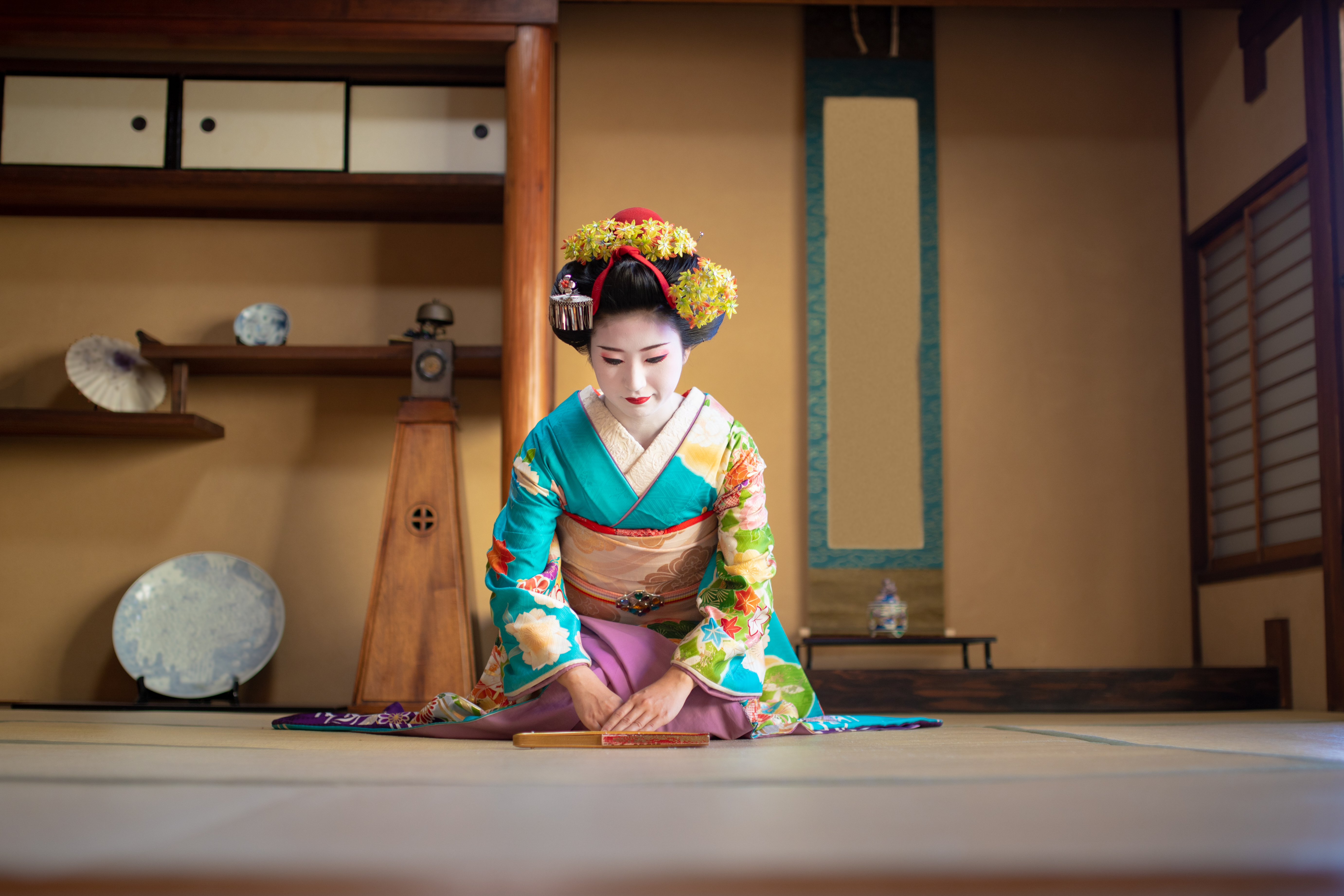 A maiko kneeling formally on tatami, hands together, in a quiet ozashiki room