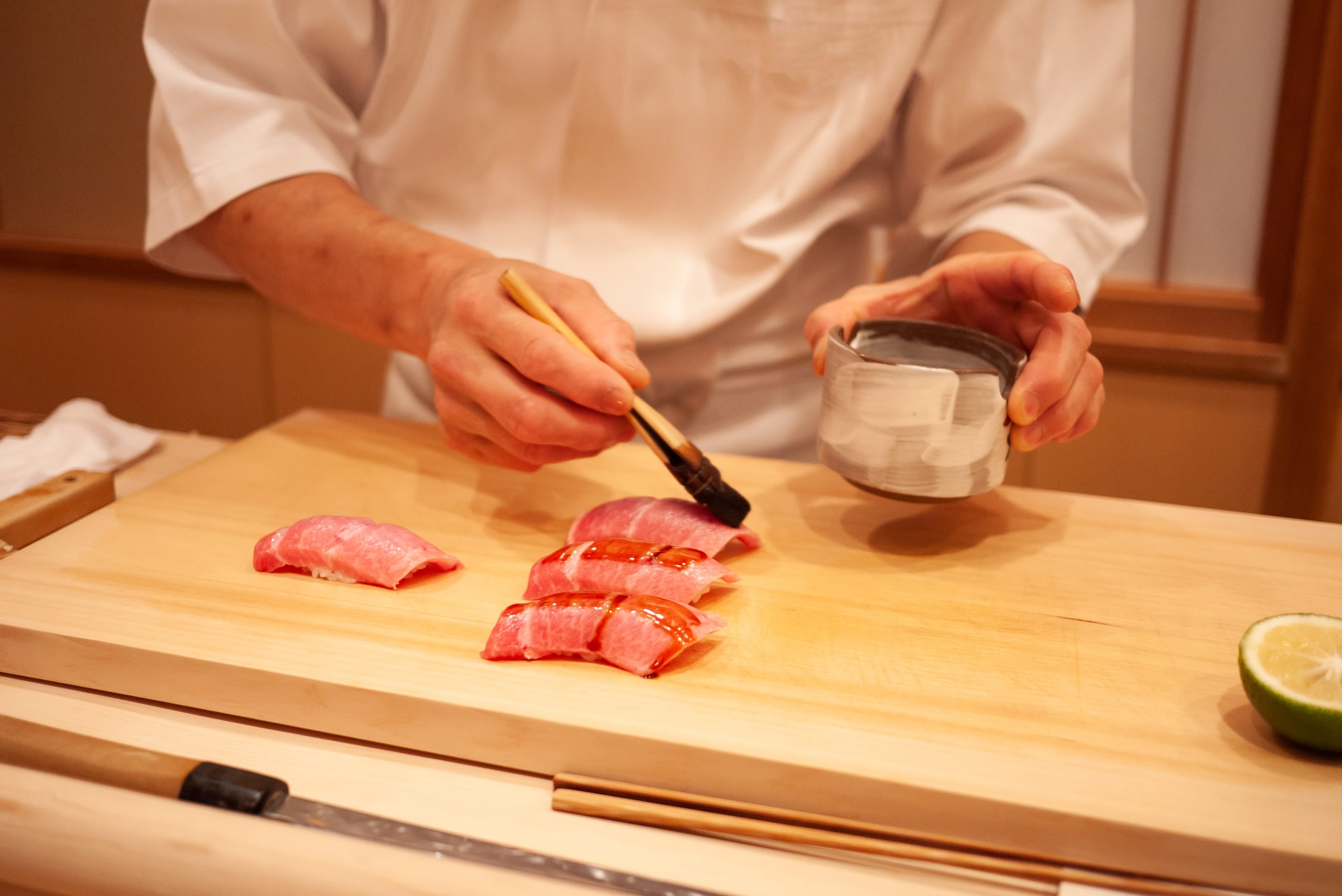 A sushi chef brushing sauce onto a piece of fatty tuna