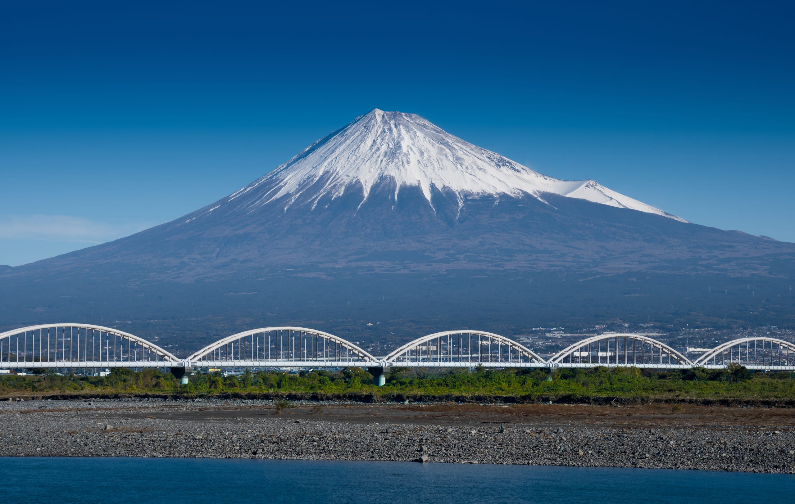 Snow-capped Mount Fuji rising beyond a white arched railway bridge