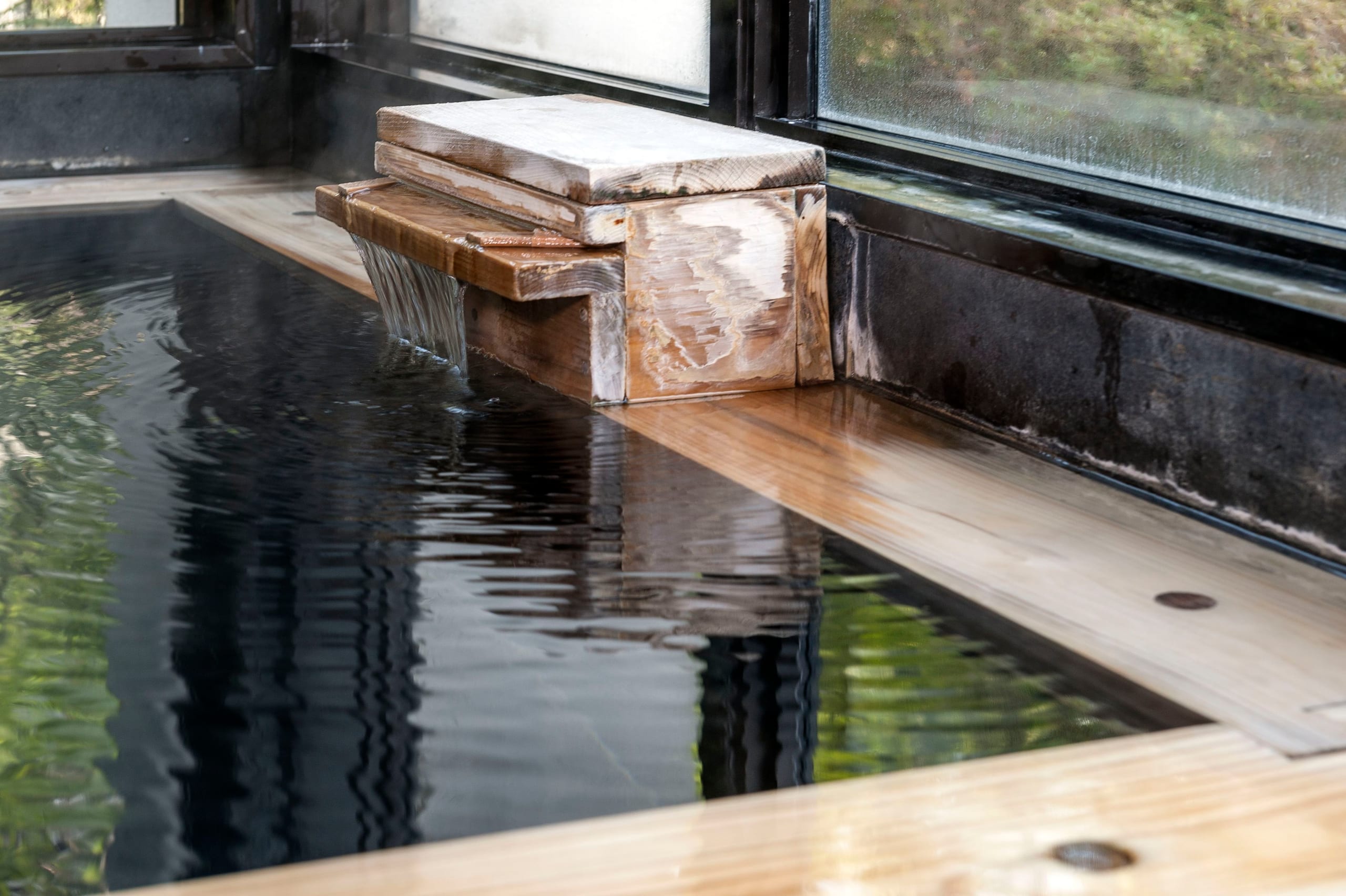 A wooden spout feeding hot spring water into a dark bath