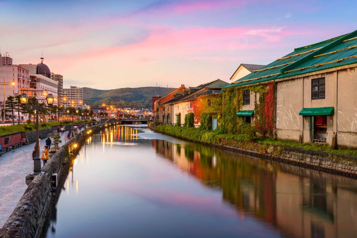 Ivy-covered stone warehouses along Otaru canal reflected in still water under a pink sunset sky