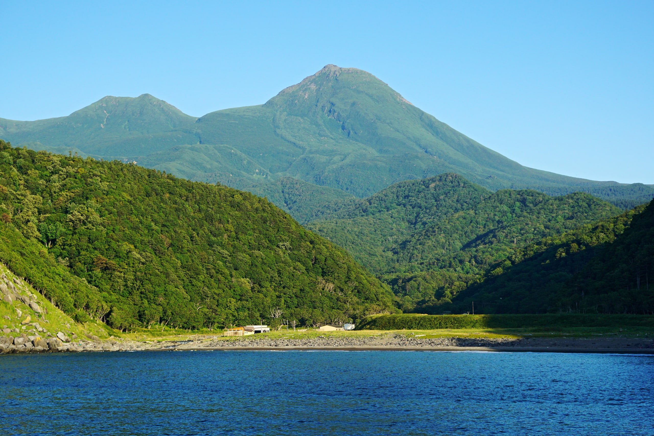 Mount Rausu rising green above the Okhotsk shore of the Shiretoko peninsula, seen from the sea in summer