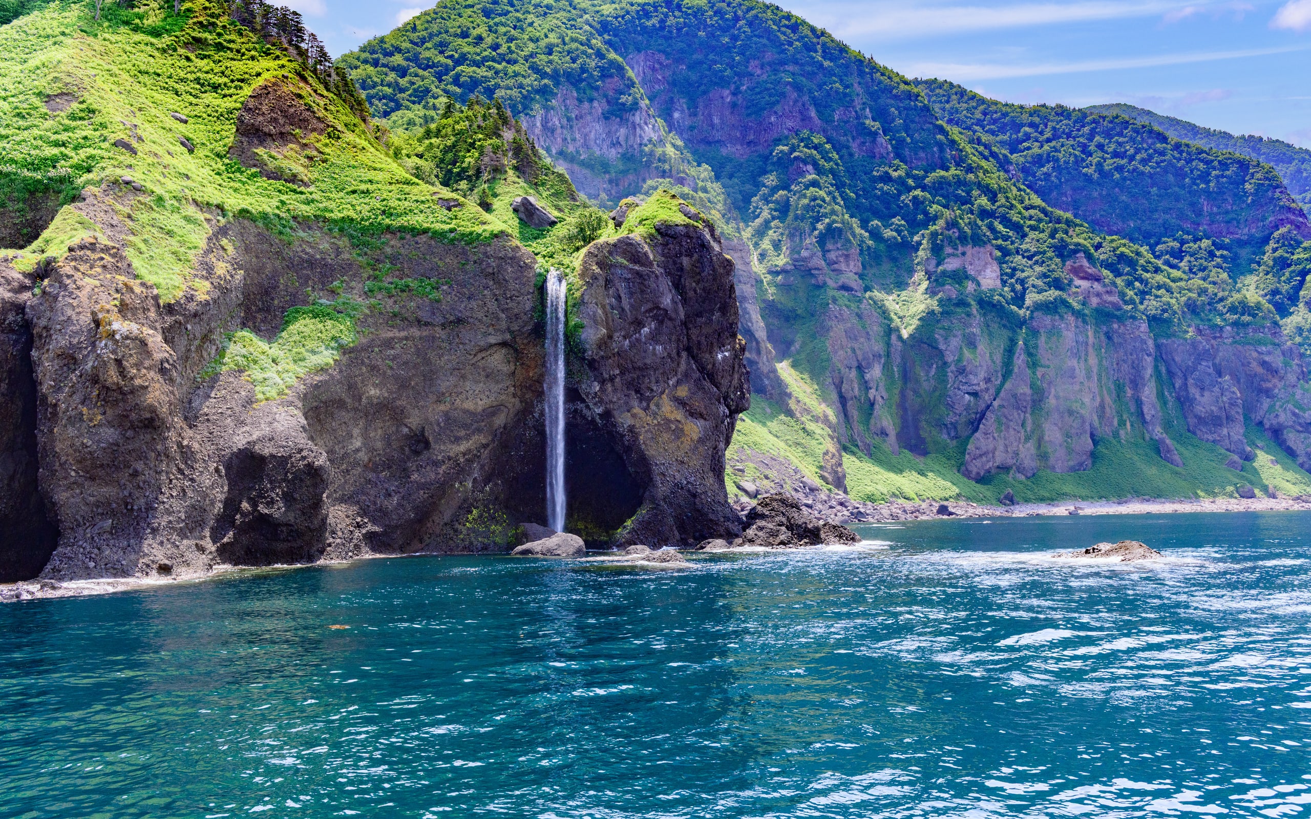 A waterfall dropping off a basalt cliff straight into the sea on the Shiretoko coast, seen from the water