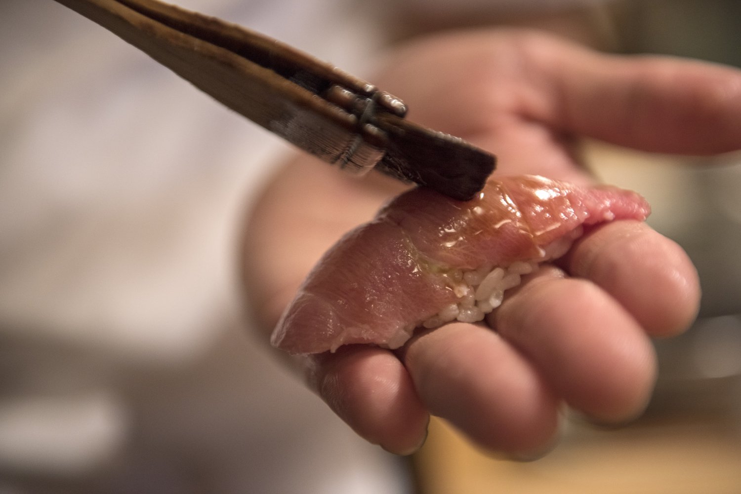 A sushi chef's hand holding a piece of tuna nigiri as a brush glazes it